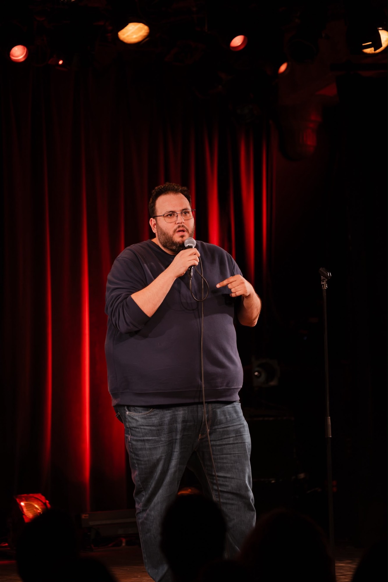 Fouad on stage with a microphone in front of a red curtain